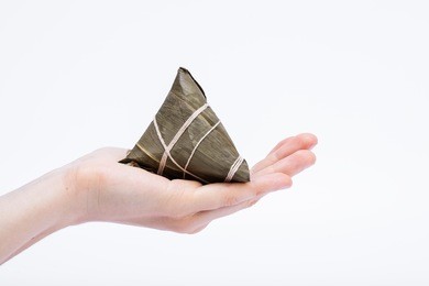 chinese sticky rice dumplings (zongzi) on women hand, made of rice and bamboo leaf, usually eaten during dragon boat festival, isolated with white background, 