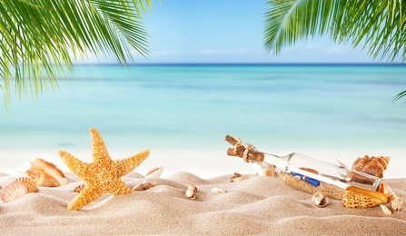 tropical beach with various shells and glass bottle with message in sand, copyspace for text. concept of summer relaxation