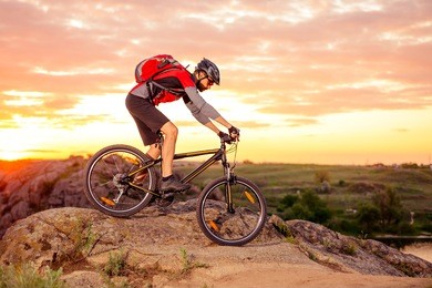 cyclist riding the bike down hill on the mountain rocky trail at sunset. extreme sports