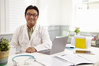 male doctor sitting at desk working at laptop in office