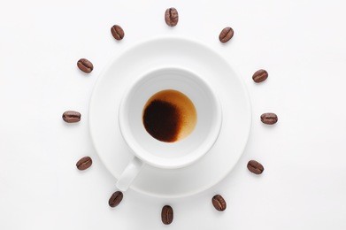 drunk cup of natural coffee on saucer and coffee beans against white background forming clock dial viewed from above