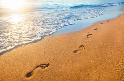 beach, wave and footprints at sunset time