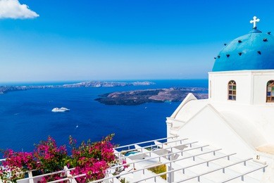 beautiful blue dome church with blooming bougainvillea and view of voclanic caldera in imerovigli, santorini island, greece