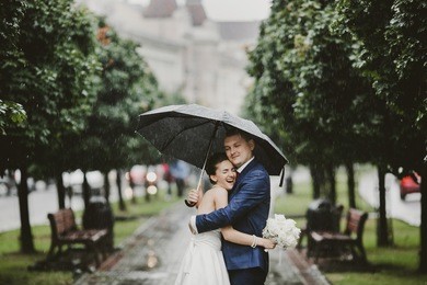 bride hugs groom and smiles standing in the rain under an umbrella