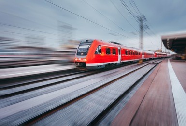 railway station with modern high speed red passenger train at sunset in nuremberg, germany. railroad with motion blur effect vintage toning. industrial landscape