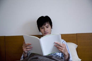 young man reading a book on the bed