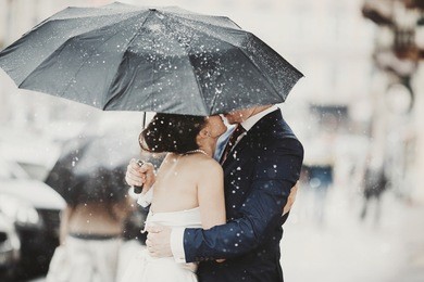 groom hides a bride behind an umbrella while kissing her