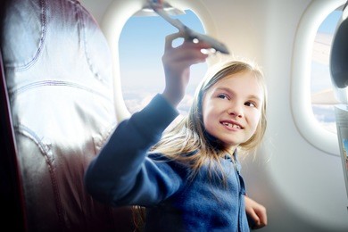 adorable little girl traveling by an airplane. child sitting by aircraft window and playing with toy plane.