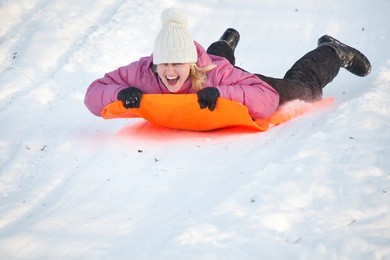 girl sledging down hill, bright and joyful winter scene