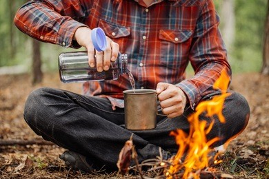 man traveler pours water from a bottle into a metal mug. bushcraft, adventure, travel, tourism and camping concept.