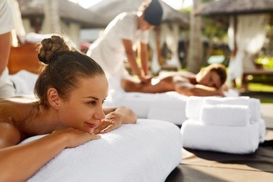 spa couple massage. beautiful happy smiling woman and healthy man enjoying relaxing body massage treatment outdoors at beauty salon. people at romantic day spa resort. health care and relax concept