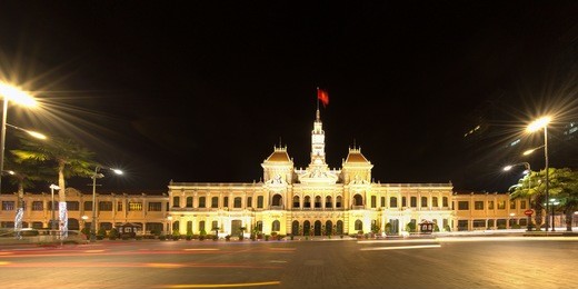 ho chi minh city hall with red flag in ho chi minh city, vietnam at night. it is known as ho chi minh city people's committee head office, was built in 1902-1908. tourist attraction, famous landmark.