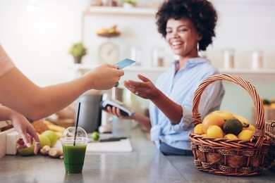 shot of a female juice bar owner taking payment from customer. female customer paying for juice with credit card.