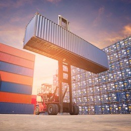 forklift truck lifting cargo container in shipping yard or dock yard against sunrise sky with cargo container stack in background for transportation import,export and logistic industrial concept