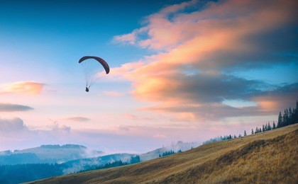 paraglide silhouette flying against the sunset sky over carpathian foggy mountains.