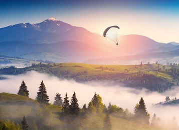 paraglide silhouette in a light of sunrise above the misty carpathian valley.