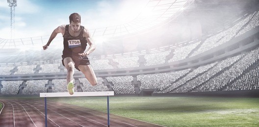 sportsman practising hurdles against view of a stadium