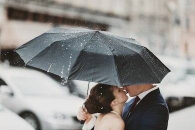 rain falls on the umbrella which hides a kissing couple