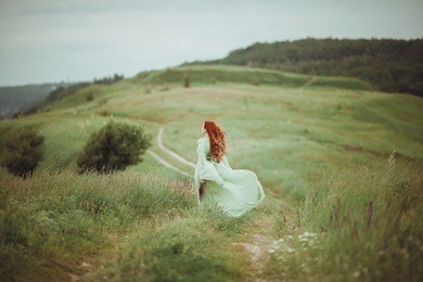 young redhead girl in medieval dress walking through field with sage flowers. freedom concept. fantasy. wind
