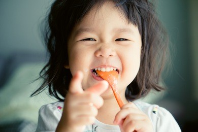 happy little asian girl eating yogurt and she have spoon in her mouth.