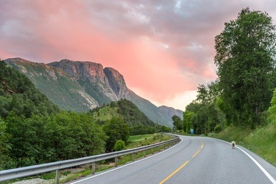 sunset over a mountain road in norway - orange skies, road into the mountains, a tiny sheep on the road