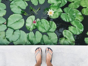 selfie of feet in sandals shoes on pavement with lotus flower pond background, top view