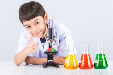 little scientist boy with microscope and colorful flask on white table