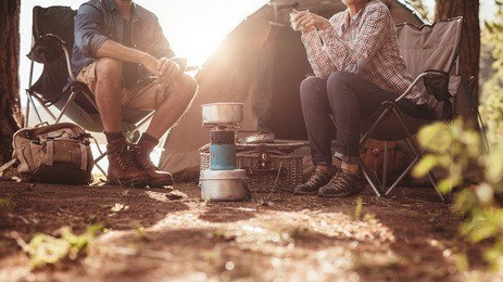 cropped image of man and woman sitting in chairs outside the tent. couple camping in forest.