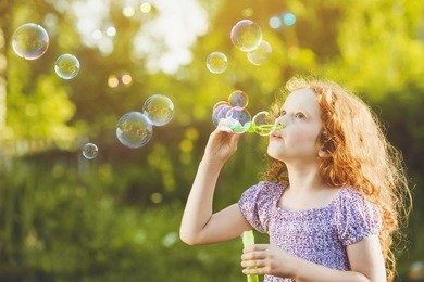 little girl blowing soap bubbles in summer park. background toning for instagram filter.