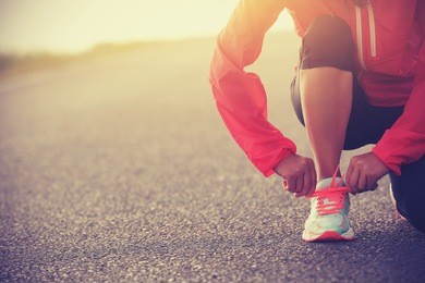 young woman runner tying shoelace on country road