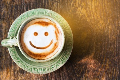 smile of latte coffee with sunshine on wooden background.(top view)