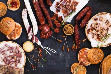 overhead view of cured meats, sausage with mustard sauce on rustic dark table. picnic concept.