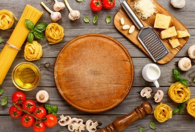 spaghetti and fettuccine with ingredients for cooking pasta on wooden table with blank of round wooden kitchen board, top view. rustic style. flat lay