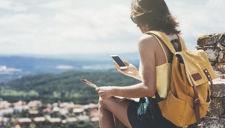 hipster young girl with bright backpack looking at a map. view from back of the tourist traveler on background mountain, sea. mock up for text message. female hands using smartphone, holding gadget