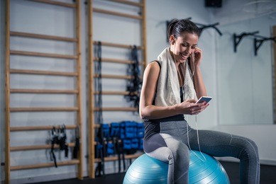 woman listening to the music while sitting on a exercise ball in the gym.