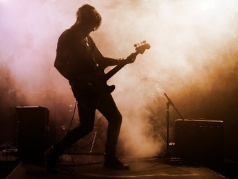 rock band performs on stage. guitarist, bass guitar and drums. the guitarist plays solo.