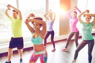 fitness, sport, dance and lifestyle concept - group of smiling people with coach dancing zumba in gym or studio