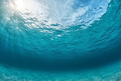 underwater shoot of an infinite sandy sea bottom with clear blue water and waves on its surface