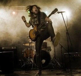 rock band performs on stage. guitarist, bass guitar and drums. the guitarist plays solo.