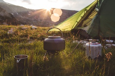 camping teapot and cap on the grass at sunrise time. mountains of bulgaria.