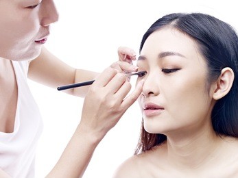 makeup artist working on a beautiful young female asian model, isolated on white background.