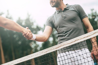 thank you for the game! low angle view conceptual image of two man in sports clothing shaking hands while standing near the tennis net on court 