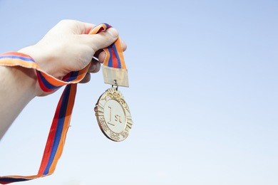 man hand raised, holding gold medal against sky