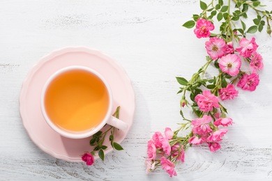 cup of tea and branch of small pink  roses on rustic table