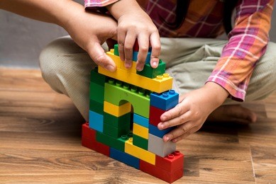 mom hand and asian kid girl building house from plastic blocks