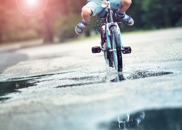 child on a bicycle at asphalt road in summer. bike in the park moving through puddle on rainy day