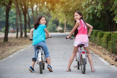 happy asian girls riding bicycle together in the park.
