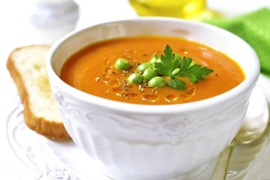 carrot creamy soup with green pea in a white vintage bowl on a