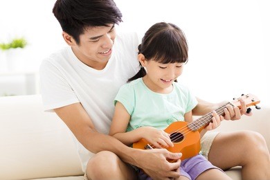 happy father teaching daughter to play ukulele