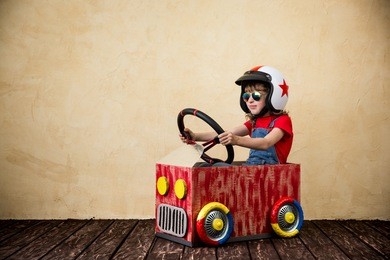 child driving a car made of cardboard box. kid having fun indoors. child playing at home. dream, imagination, childhood. travel and summer vacation concept